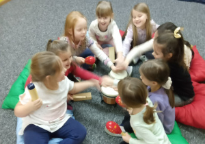 Grupa dzieci siedzi w kole i trzymają swoje ręce na podwójnym bębenku.